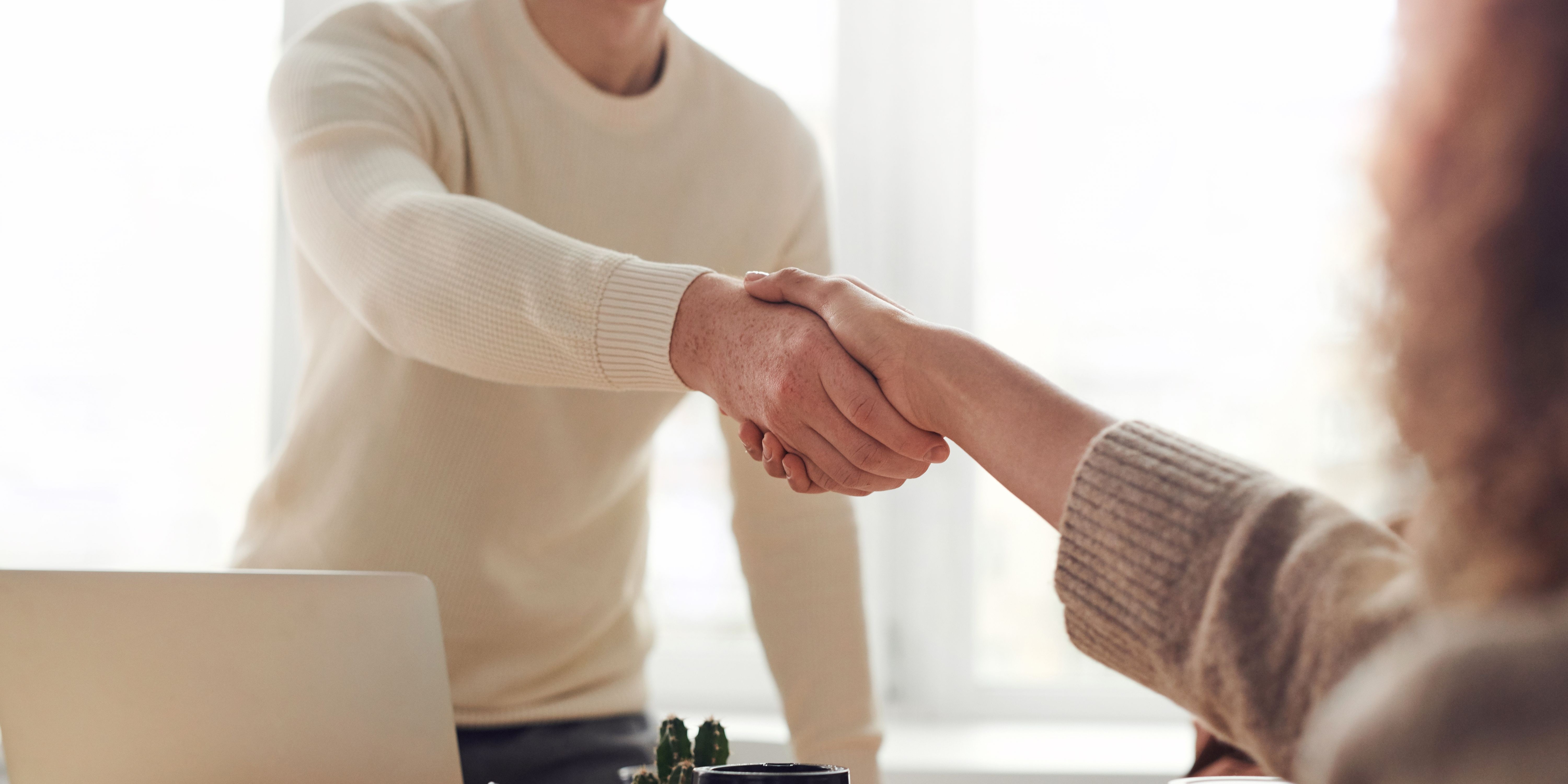 Stock photo of two people shaking hands over a desk.