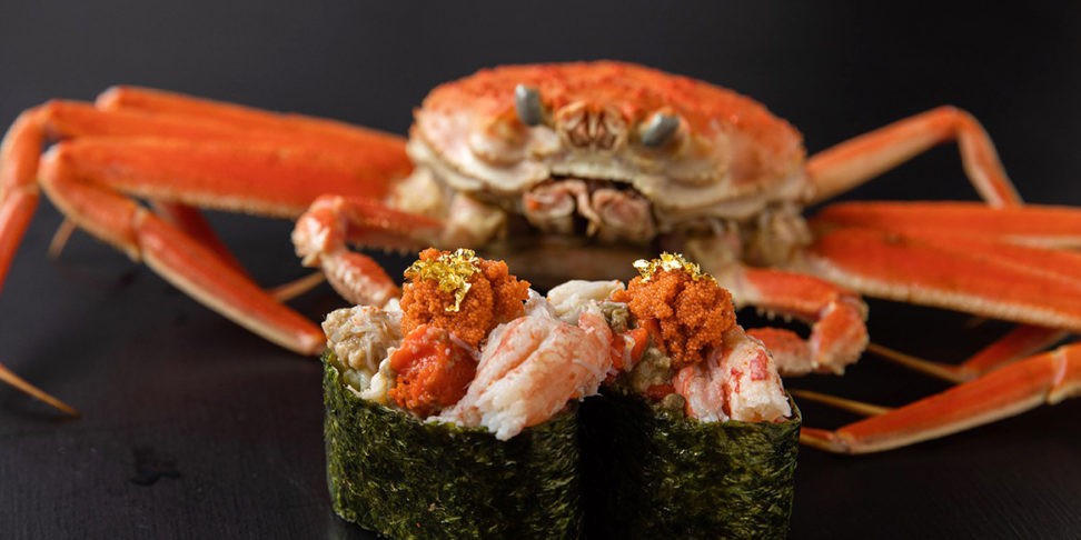 Closeup photo of two crab sushi, with a large snow crab in the background.